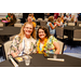  Two women at a table. One has an orange flower in her hair, and the other is wearing an orange lei. 