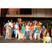  A huge group of eighteen people standing on stage to pose with their Hawaiian themed clothing. 