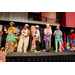  Individuals in various Hawaiian themed outfits lined up on stage laughing. 