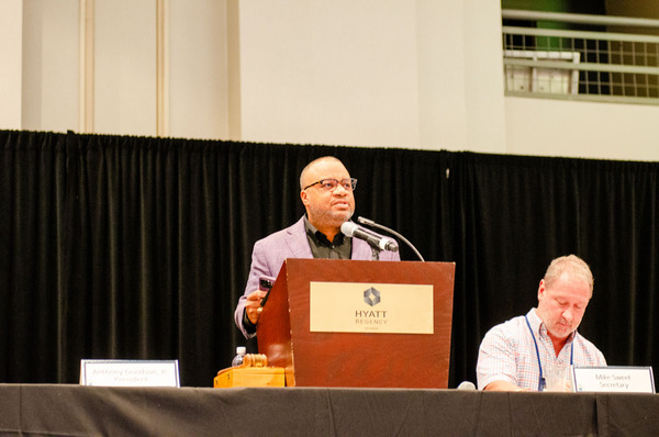 Anthony Goodson speaking at the podium, while Mike Sweet sits next to him.