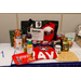  A view of raffle basket Number 9. This basket has Georgia themed items including a Georgia bamboo cutting board, a 20 oz Stainless Steel Georgia Tumbler, an Atlanta Braves beach towel, a Georgia scented candle, a Coca Cola tin tray, blueberry pepper jelly, deep fried peanuts, gift cards, and a Georgia hat. 