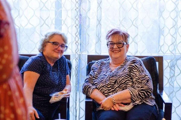 A woman in a zebra print shirt sitting and smiling with a woman in a blue and white polka dot shirt.