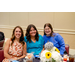  Two woman in blue shirts sitting with a woman in a brown and white floral dress. 