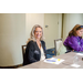  A woman in a black shirt that says, Gloria, Executive Director, smiling while sitting at a table. 