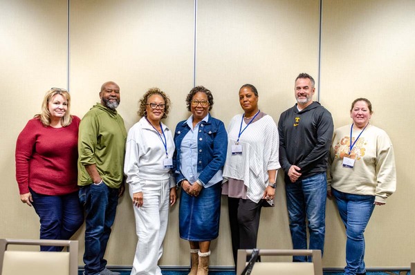 Seven individuals lined up along a wall for a group photo.