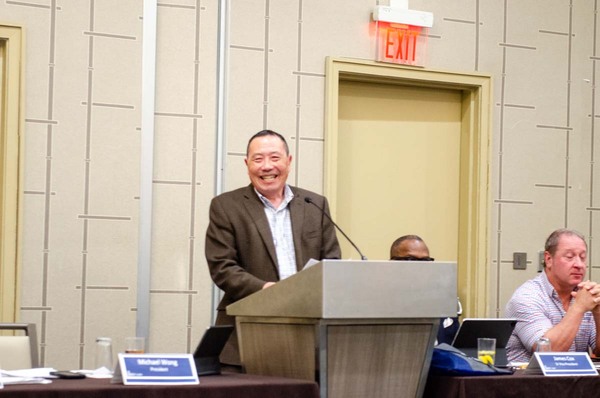 Michael Wong smiling while standing behind a podium.