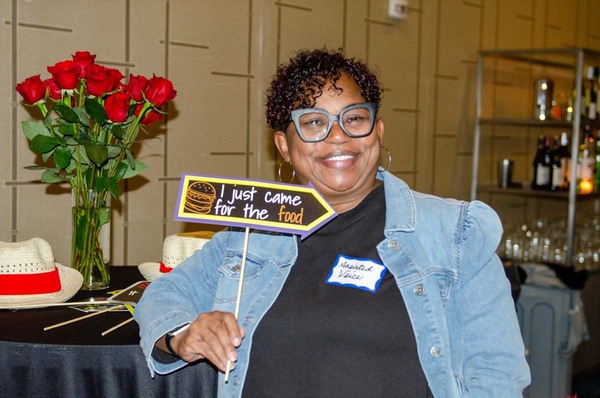 A woman with a name tag that says Anointed Voice holding a sign that says I just Came for the Food.