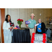  Three individuals standing around a bar table holding signs. The signs include, It Wasn't Me, I Suspect Foul Play, and Too Pretty For Murder. 