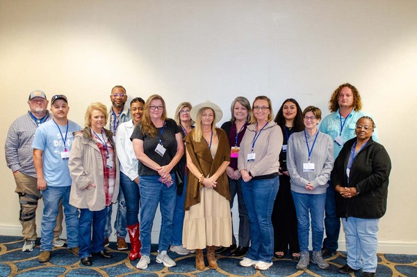 Fourteen individuals posing for a group photo in front of a wall.