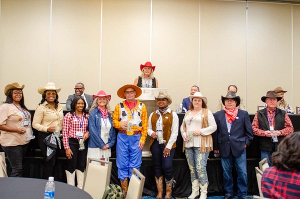 Nine individuals in cowboy costumes standing in front of the stage with speakers on it.
