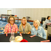  Three women smiling while sitting around a dining table. 