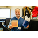  A man holding a completely blacked out bingo card and a small blue gift bag. 